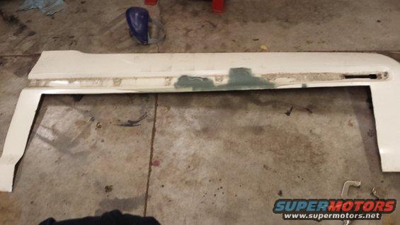 White car fender with visible body filler and damage, lying on a concrete floor