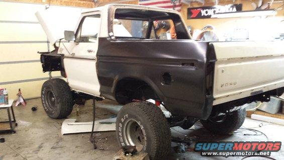 White and dark brown 1978 Ford Bronco undergoing repairs, viewed from the rear three-quarter angle