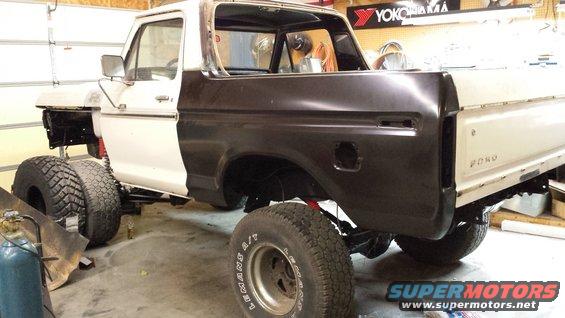 White and dark brown 1978 Ford Bronco undergoing restoration, lifted with large tires, in a garage