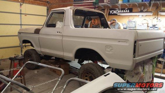 White Ford pickup truck undergoing restoration, lifted on stands in a garage