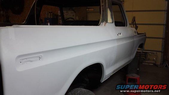 Side view of a 1978 Ford Bronco body with primer paint, undergoing restoration