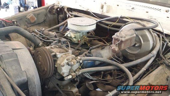 Engine bay with V8 engine, carburetor, and air filter. Visible AC compressor and brake booster