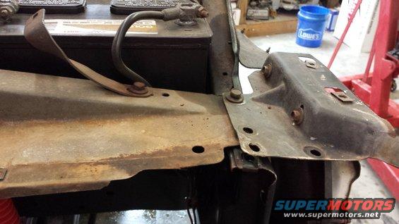 Car battery and rusty metal brackets under a hood