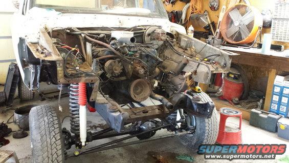 1978 Ford Bronco chassis in garage, front end disassembled, engine bay empty, red shock absorbers visible