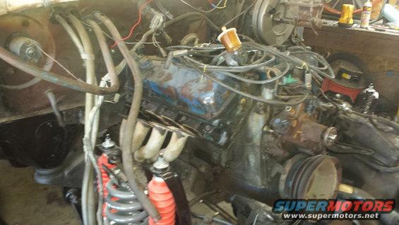 engine bay with V8 engine, hoses, and wiring. Some red shocks visible