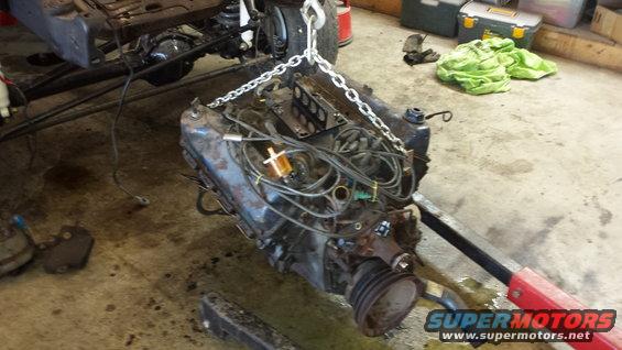 Engine suspended by a chain hoist, with vehicle frame and suspension visible in background