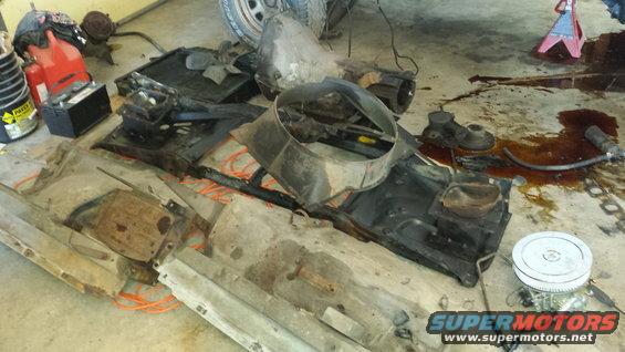 Disassembled vehicle parts including radiator, transmission, and engine components on a concrete floor