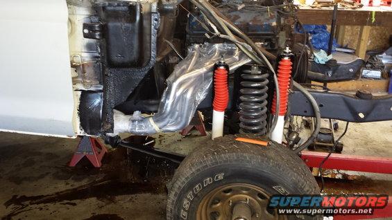 1978 Ford Bronco chassis on jack stands, showing engine, exhaust headers, and red-shocks
