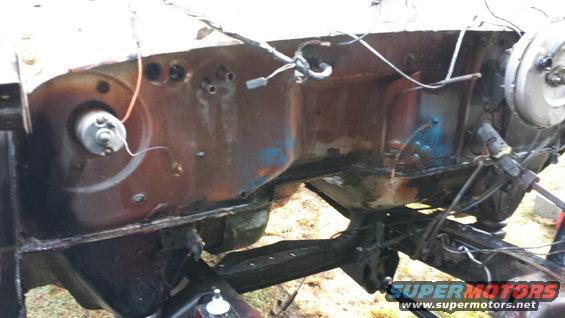 Engine bay of a disassembled vehicle, showing rusted metal, wires, and brake booster