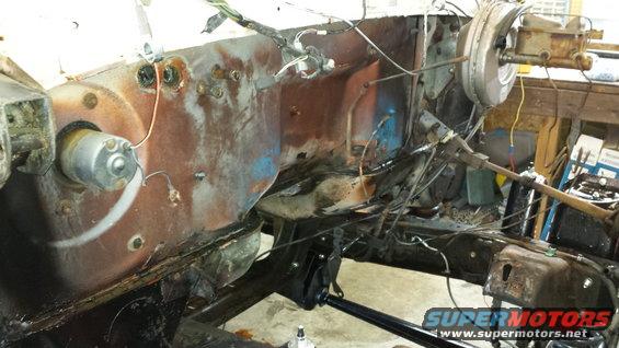 Disassembled vehicle firewall with rusted metal, wiring, and brake booster visible