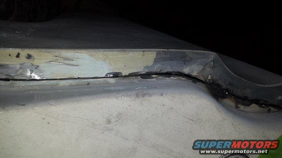 Close-up of a dented and repaired vehicle body panel with visible welds and primer