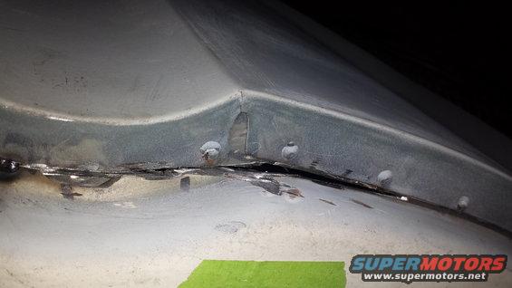 Metal panel seam with rivets and visible rust, partially covered by green tape