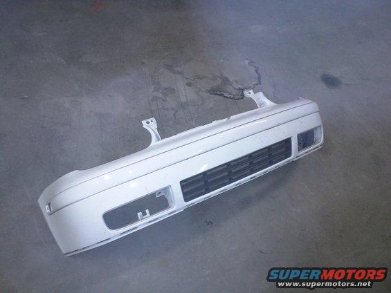 White front bumper with grille and fog light openings, resting on a concrete floor