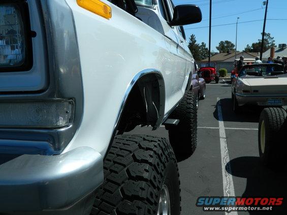 Side view of a lifted white pickup truck with large tires. Other vehicles are parked nearby