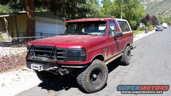 Red Ford Bronco with aftermarket bull bar and winch, lifted suspension, and off-road tires parked on a street