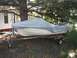 1963 Lund WC 14 - A boat on a trailer is covered with a tarp and parked in an outdoor setting with trees and a building in the background.