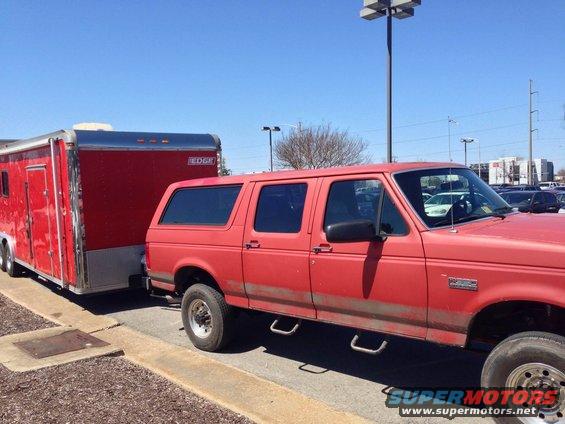 Red SUV with four doors towing a red trailer. It has running boards and a side view