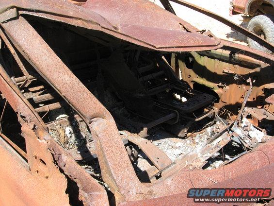 Interior of a rusted-out vehicle showing damaged seats and frame