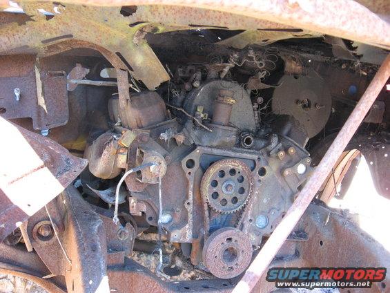 Heavily rusted engine block with timing gears visible. Some body panels and wiring are also present