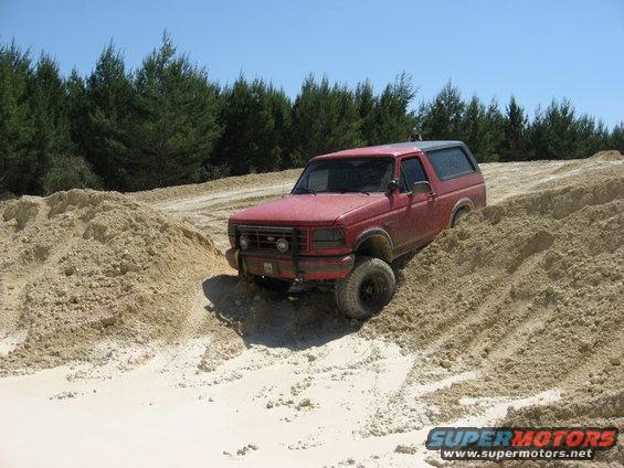 Red 1994 Ford Bronco navigating a sandy off-road trail