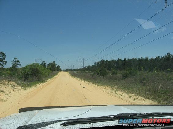Driving down a sandy dirt road with power lines overhead and trees on either side