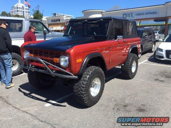 Red 1979 Ford Bronco with black hood, custom bumper, and large off-road tires parked next to another vehicle