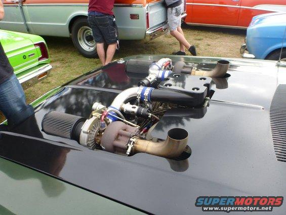 Car hood with twin turbochargers and intercooler piping. Other cars visible in background