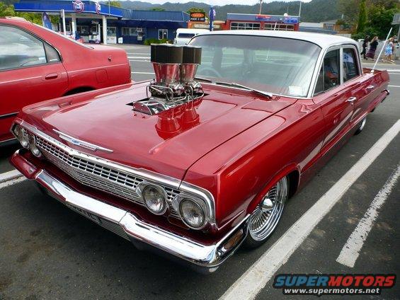 Red 1963 Chevrolet Impala with a blown V8 engine and chrome wheels parked next to a red sedan