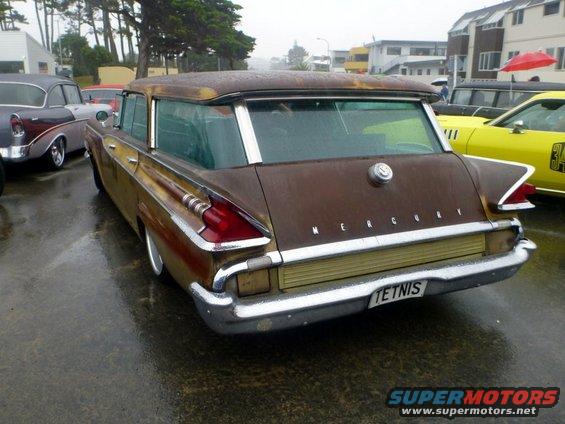 Brown Mercury wagon with fins and chrome bumper. License plate says TETNIS. Other cars are parked nearby