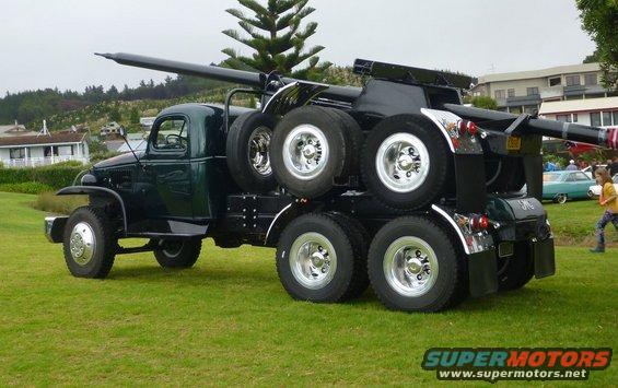 Dark green heavy-duty truck with a boom and multiple tires, parked on grass