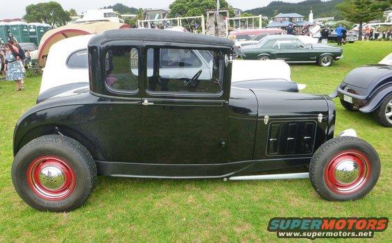 Black hot rod coupe with red wheels and chrome hubcaps, seen from the side