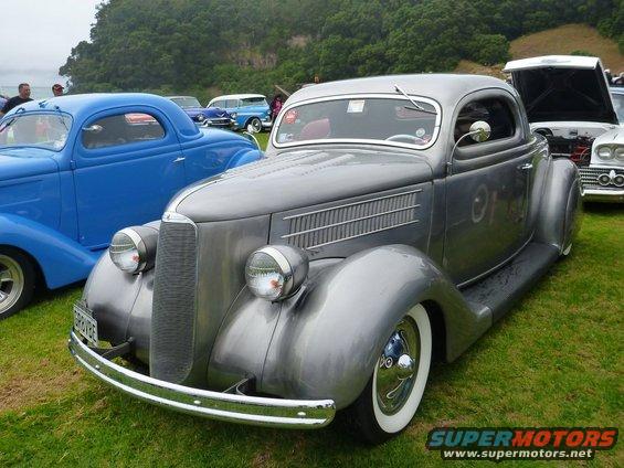 Gray 1935 Ford Coupe hot rod with whitewall tires parked on grass, blue coupe in background