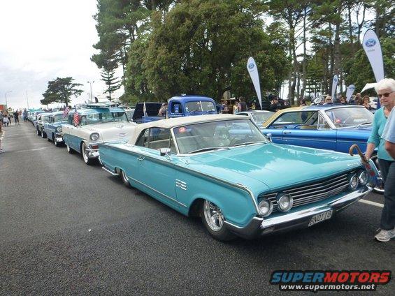 Turquoise convertible with chrome grille and side trim, parked in a line of cars