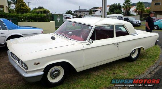 White sedan with a scoop on the hood parked on grass. Another car is to its left