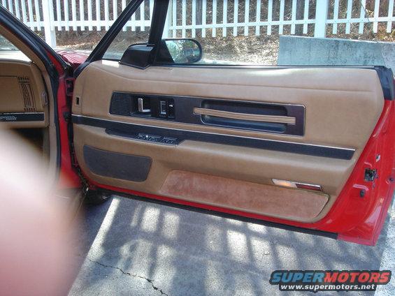 Red car interior door panel with tan upholstery, power window controls, and a chrome handle