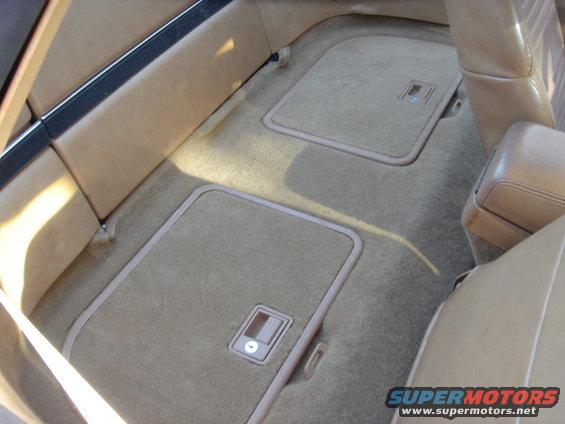 Car interior with tan carpet and two floor storage compartments