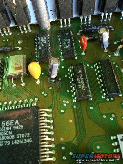 Close-up of a green circuit board with various chips, resistors, and capacitors. Some text is visible on the chips
