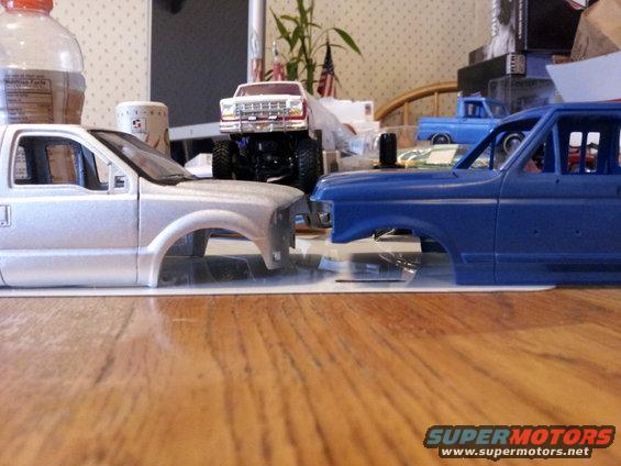 Two unpainted model truck bodies, one silver and one blue, sit on a wooden surface