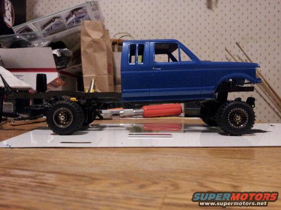 blue model truck cab on a chassis with wheels, sitting on a table with tools and boxes in the background
