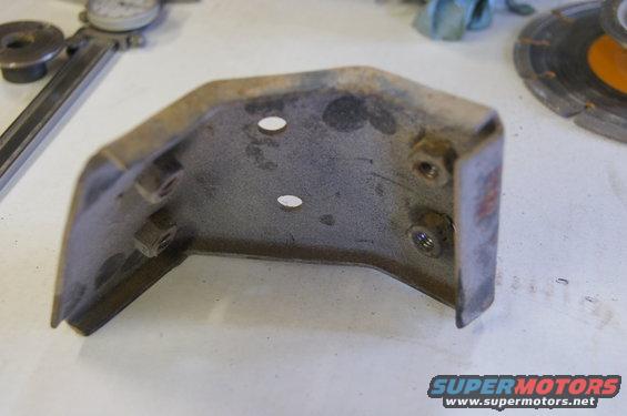 Rusty metal bracket with two bolt holes and nuts attached, on a white surface with tools