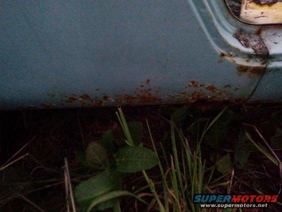 Close-up of rust on a vehicle's lower body panel near the ground