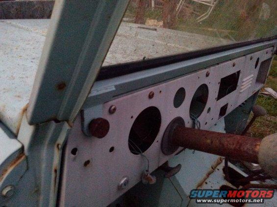 Interior view of a vehicle dashboard with multiple circular gauge cutouts and a rusty steering column