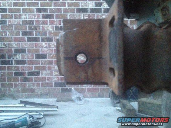 Close-up of a rusty metal bracket with a hole in it, against a brick wall