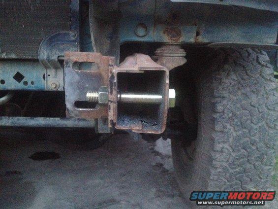 Trailer hitch receiver with bolt and nut attached to rusty metal bracket, near tire
