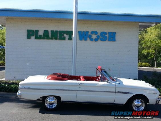White convertible parked in front of a building with 'PLANET WASH' sign. Red interior visible