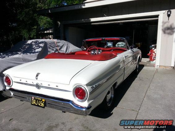 White 1963 Ford Falcon convertible with red interior parked in front of a garage