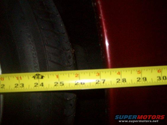 Yellow tape measure showing approximately 26 inches of clearance next to a tire and dark red car body panel