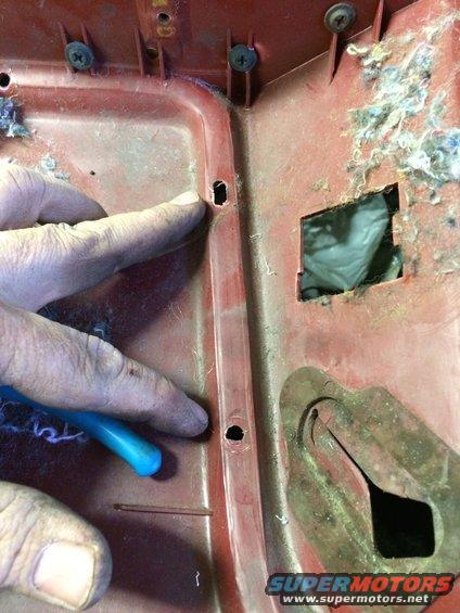 Red interior panel with screw holes, insulation, and a hand holding a blue tool
