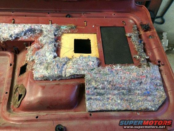 Disassembled car door panel with insulation removed, showing speaker cutout and mounting points