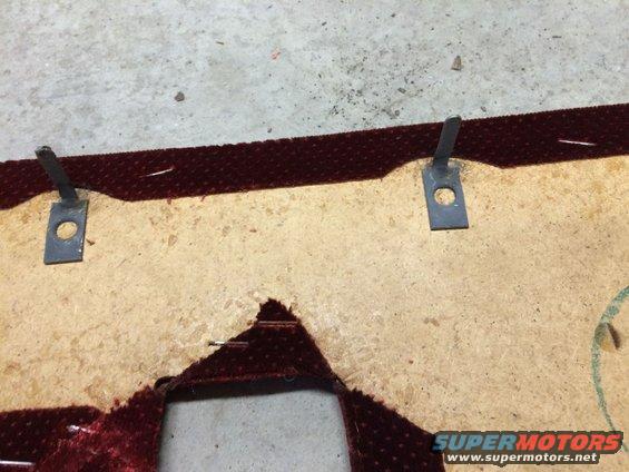 Close-up of a torn, maroon fabric-covered interior door panel with metal clips